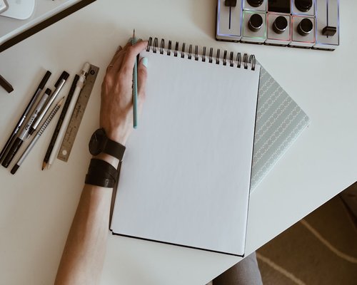 A person writing notes on a pad placed over a clean desk